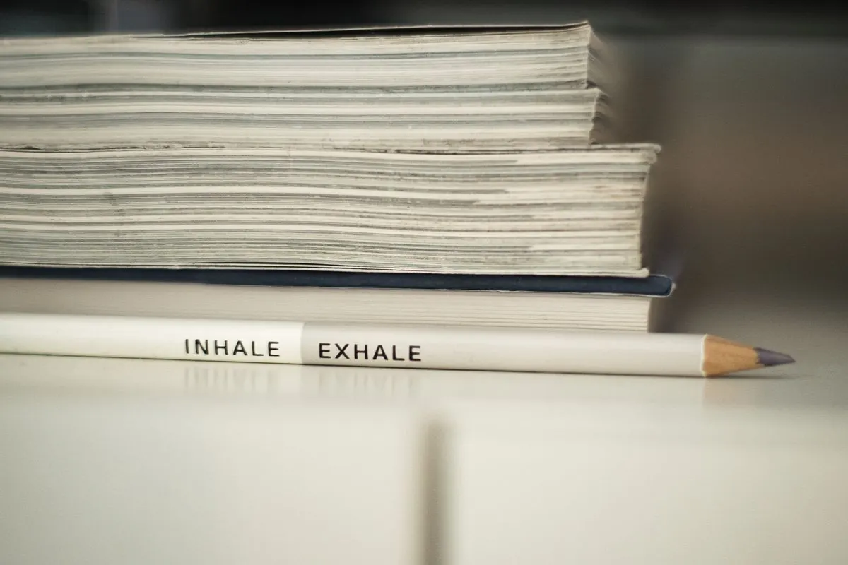 Bleistift mit der Aufschrift „Inhale – Exhale“ vor einem Bücherstapel