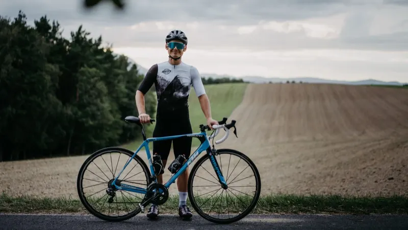 Mario Einödmaier steht lächelnd mit seinem Rennrad am Feldrand