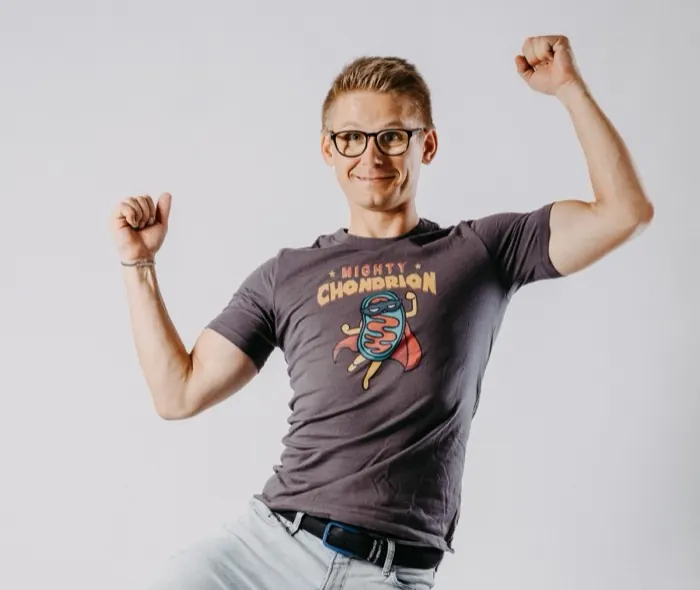 Mario Einödmaier jubelt mit erhobenen Fäusten, auf seinem Shirt der Mighty-Chondrion-Comic: ein Mitochondrium im Superheldenkostüm